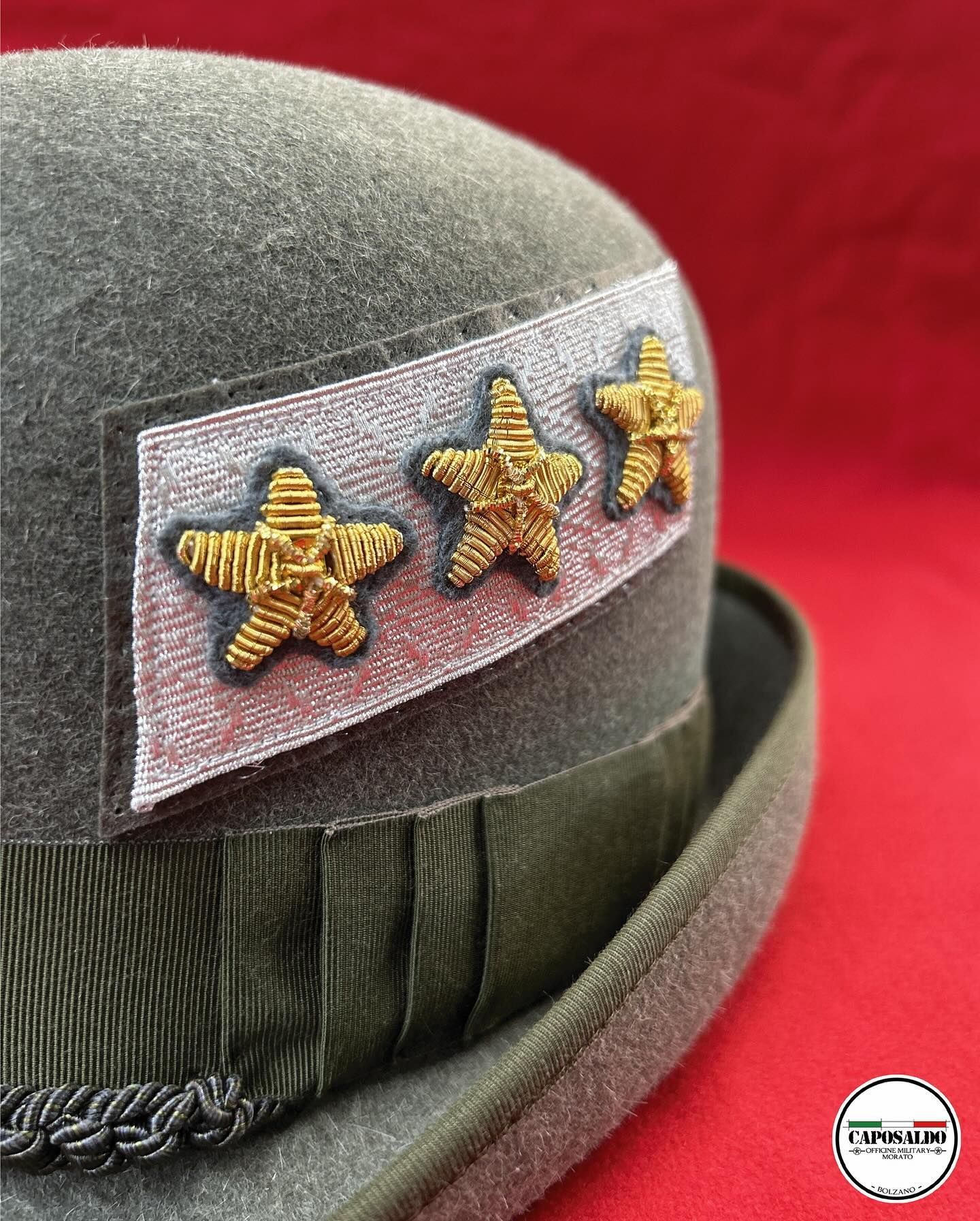 Berretto militare grigio con stella dorata su sfondo rosso.