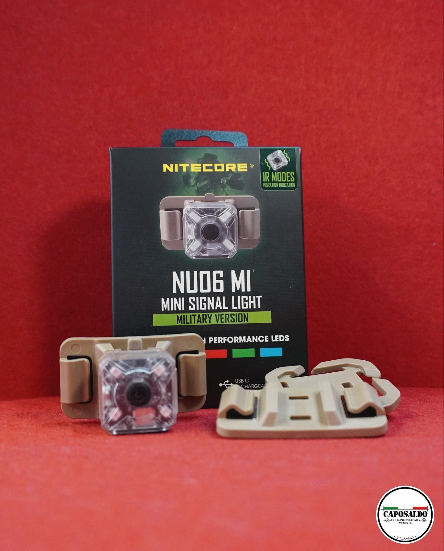 Mini torcia di segnalazione Nitecore NU06 MI nella confezione, con supporti color sabbia e una piccola luce trasparente su sfondo rosso.