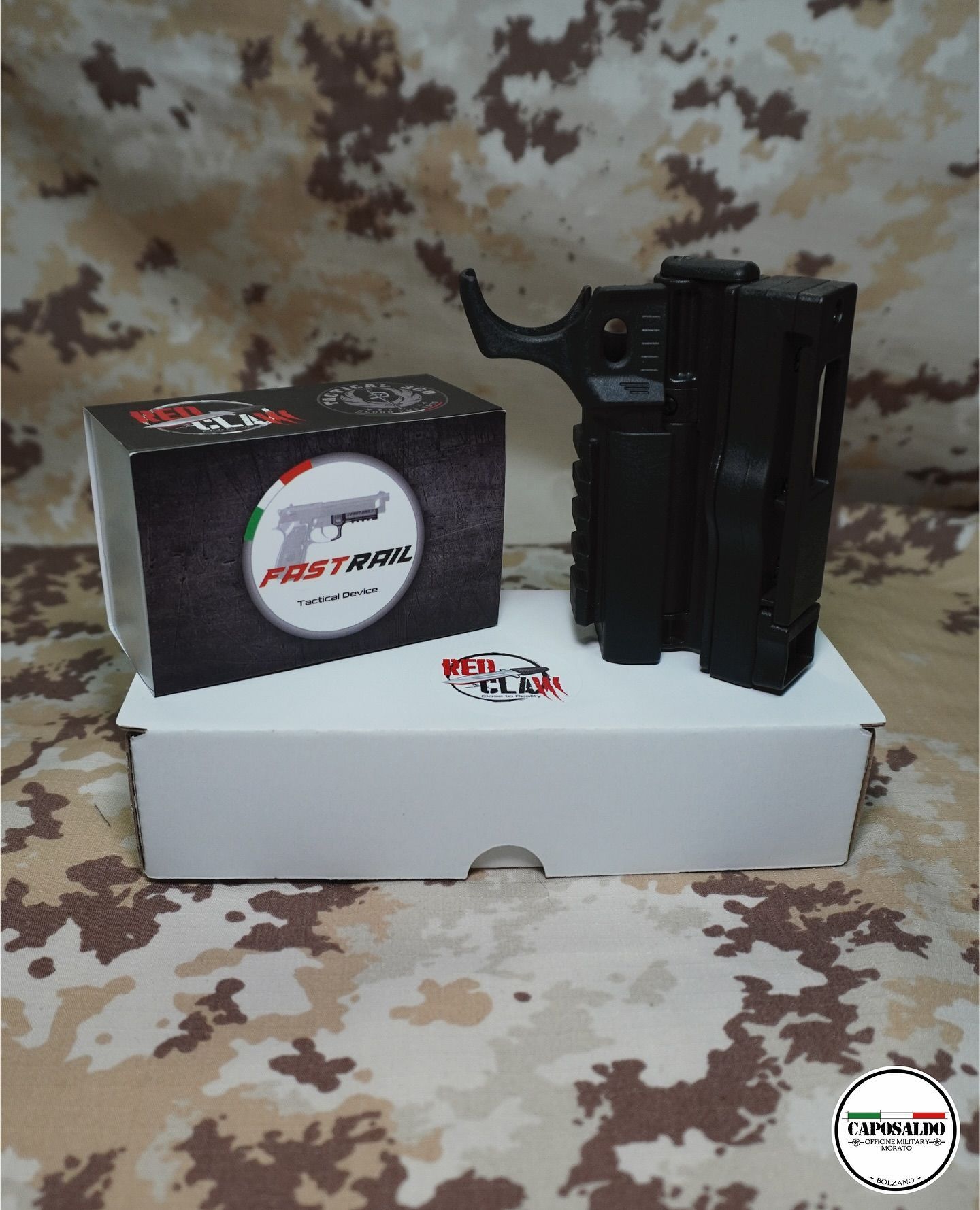 Accessorio pistola nera su scatola bianca accanto alla confezione del prodotto su sfondo mimetico