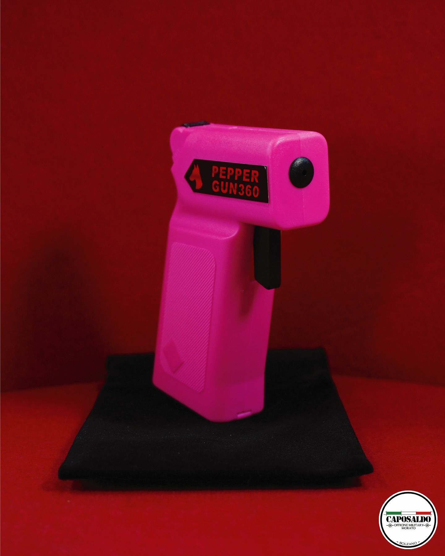 Spray al peperoncino portatile di colore rosa su un panno nero contro uno sfondo rosso.