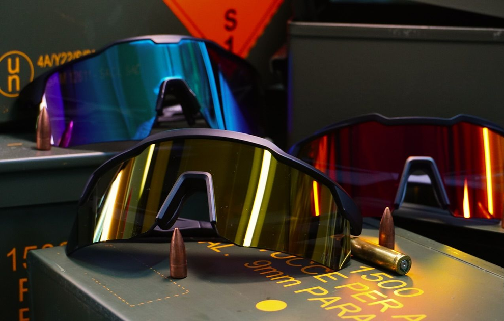 Occhiali da sole esposti sugli scaffali di un negozio, con lenti a specchio iridescenti e montature scure.