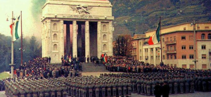 Una folla e soldati in uniforme si radunano davanti a un monumento neoclassico in una piazza cittadina.