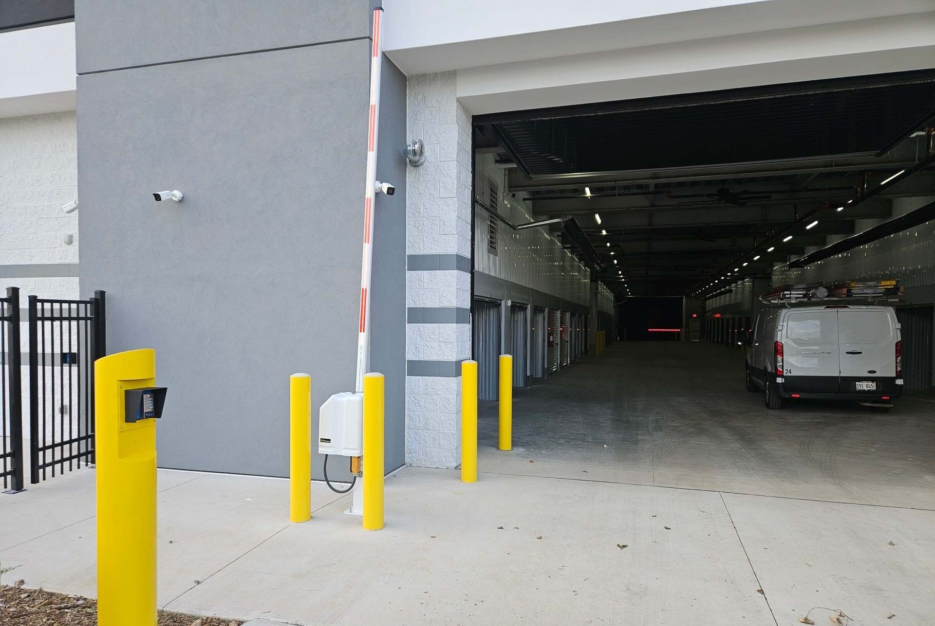Entrance to a storage facility with a gray exterior, open door, security cameras, and a white van inside.