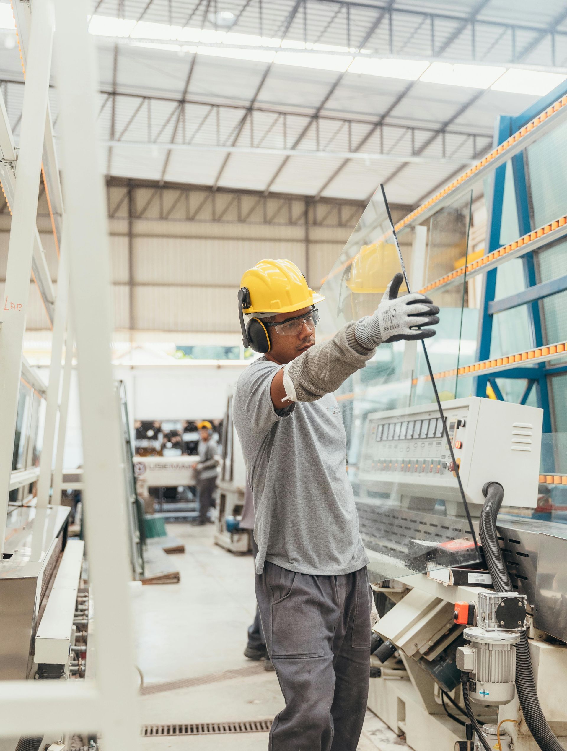 Worker in a factory with protective gear handling a large pane of glass.