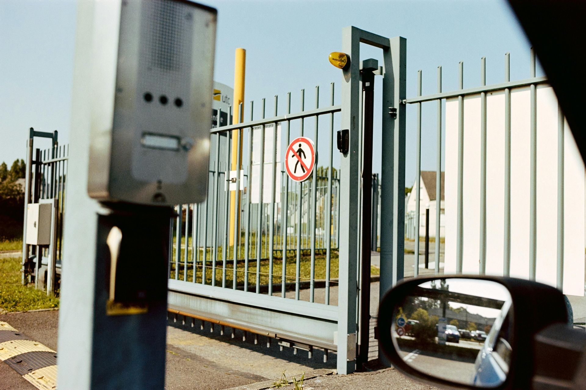 A metal gate with a no-pedestrians sign, seen from a car window.