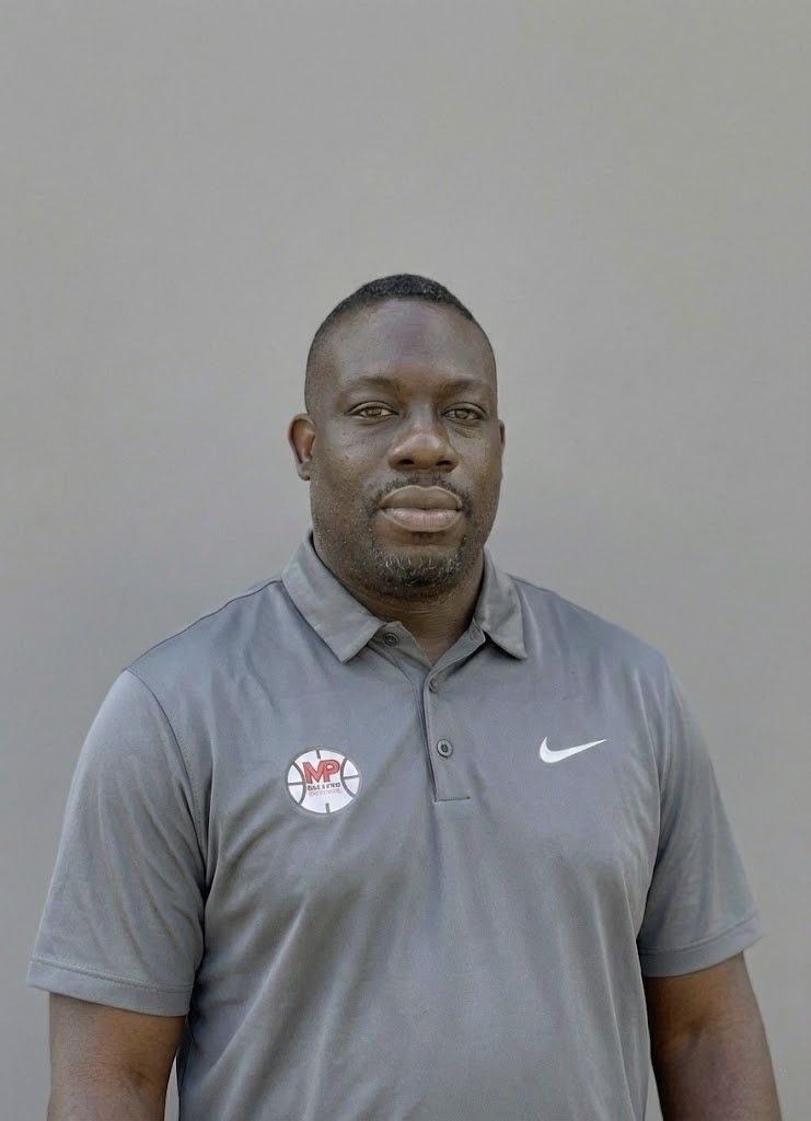 Woman with glasses, wearing a purple hat and tan coat, smiles against a gray background.