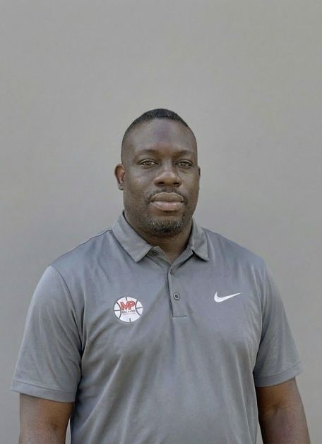 Woman with glasses, wearing a purple hat and tan coat, smiles against a gray background.