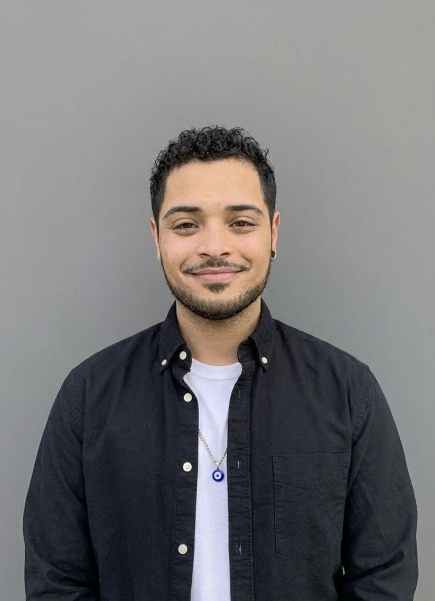 Woman with glasses, wearing a purple hat and tan coat, smiles against a gray background.