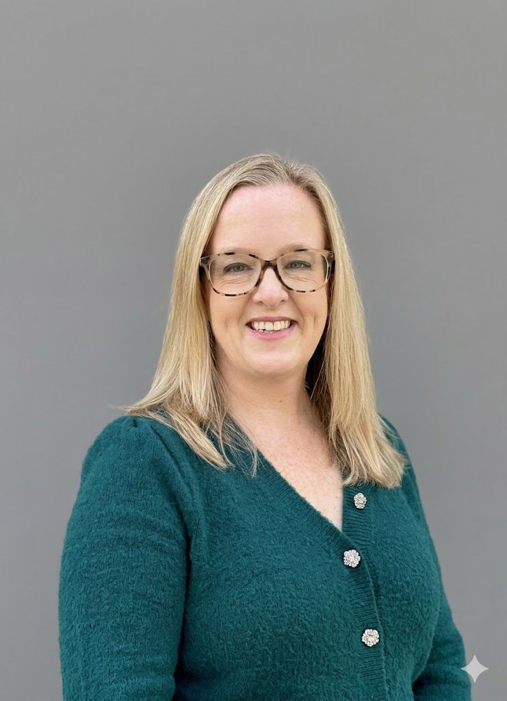 Woman with glasses, wearing a purple hat and tan coat, smiles against a gray background.