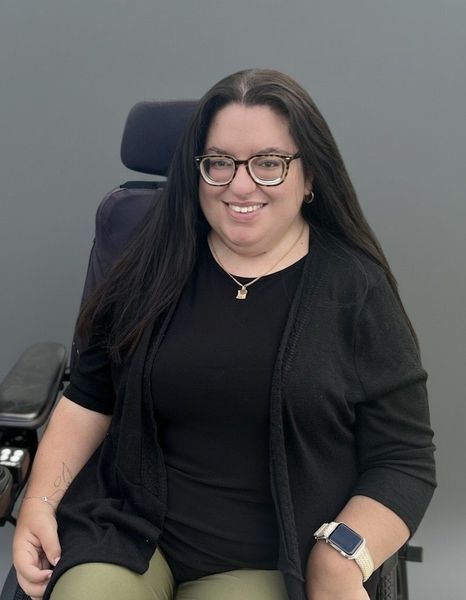 Woman with dark hair and bangs, wearing a burgundy sweater, smiling at the camera.