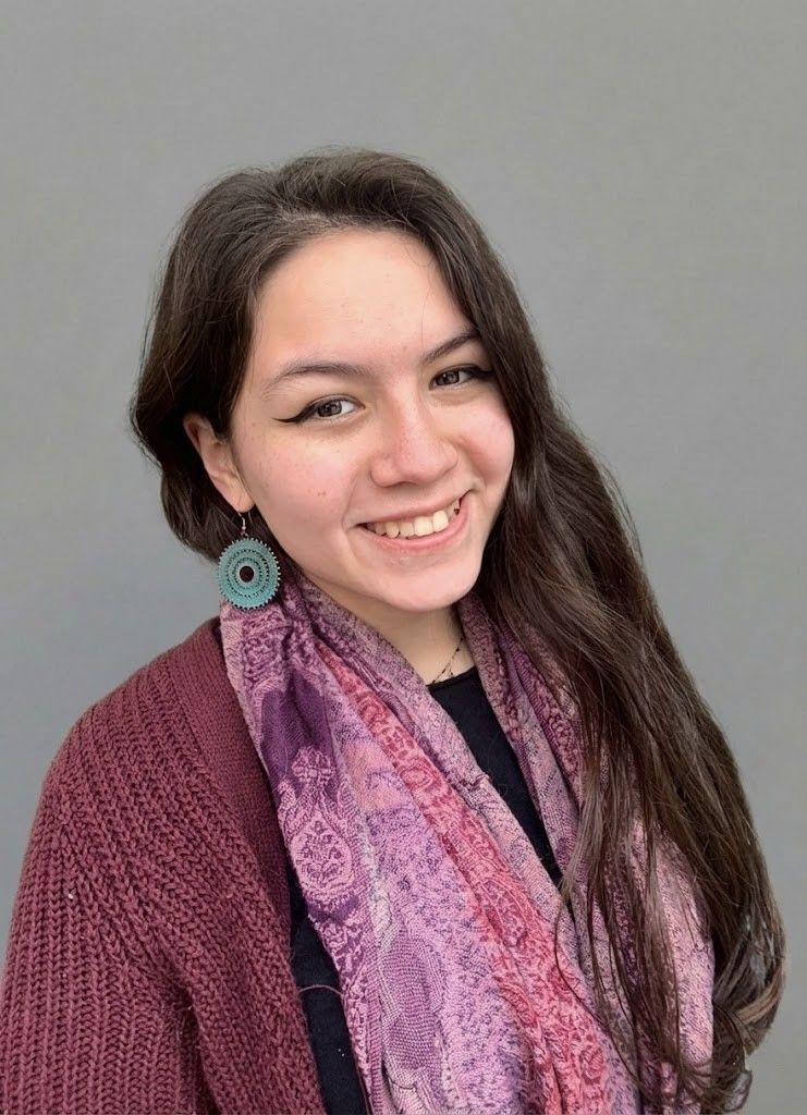 Woman with dark hair and bangs, wearing a burgundy sweater, smiling at the camera.