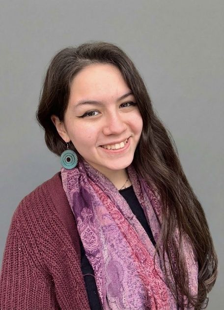 Woman with dark hair and bangs, wearing a burgundy sweater, smiling at the camera.