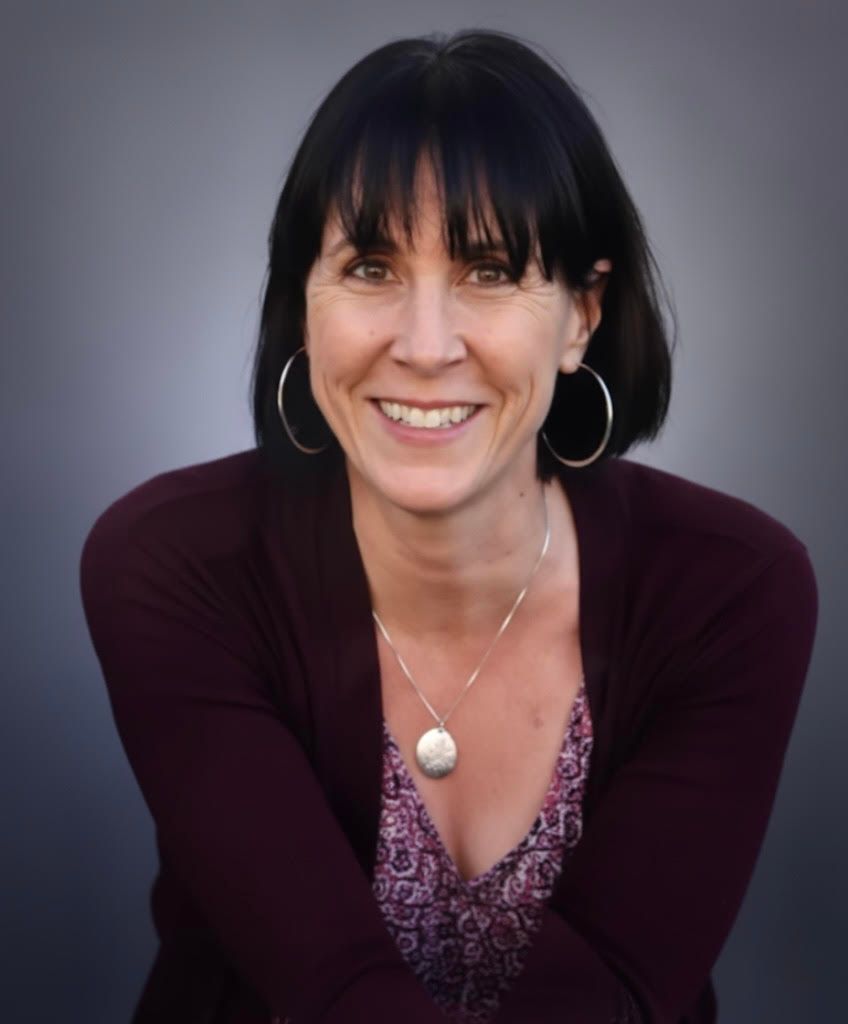 Woman with dark hair and bangs, wearing a burgundy sweater, smiling at the camera.