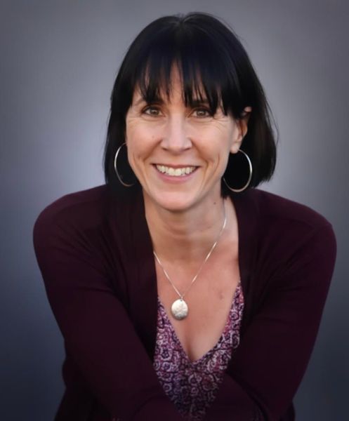 Woman with dark hair and bangs, wearing a burgundy sweater, smiling at the camera.