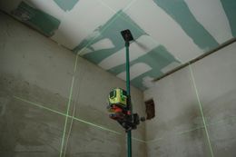 A green laser level projects lines on walls and ceiling, used for construction in a room.