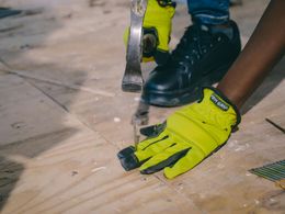 Person using a chisel to remove wood flooring, wearing safety gloves and black shoes.