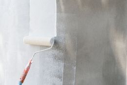 A paint roller applies white paint to a textured concrete wall.