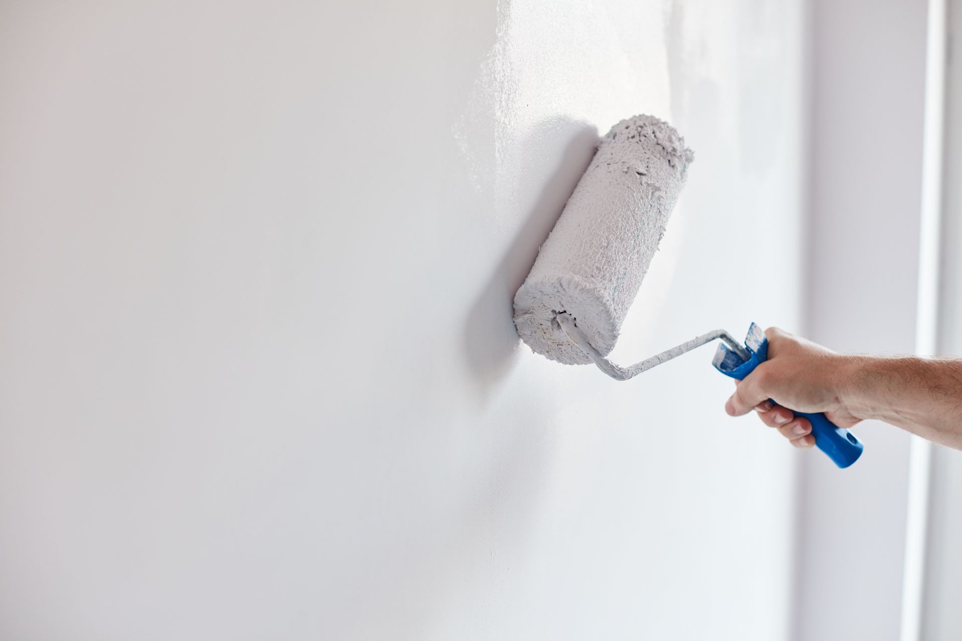 Hand using paint roller to apply white paint to a wall.