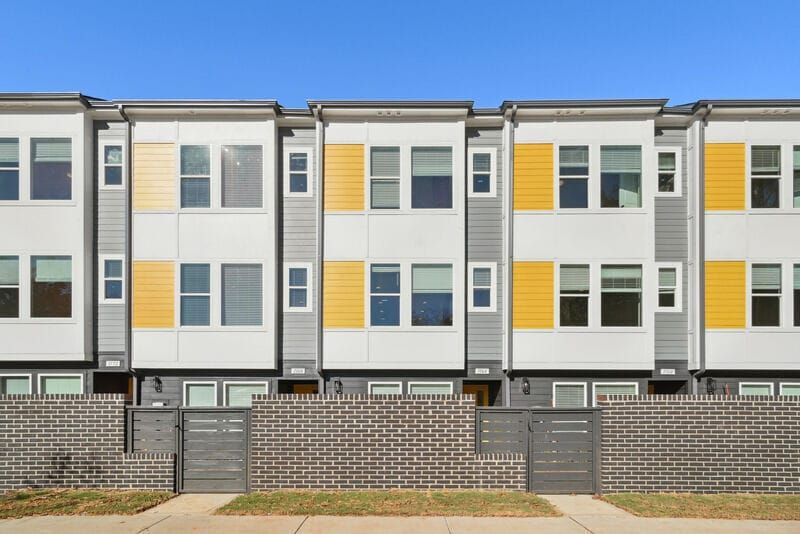 Row of modern townhouses with white and grey siding, yellow accents, and a brick wall.