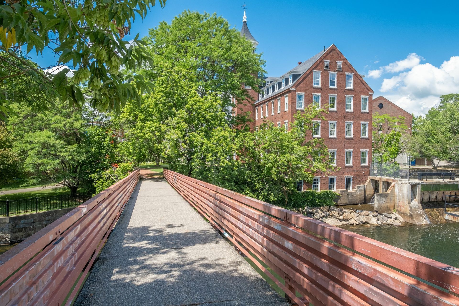 A wooden bridge over a river with a brick building in the background.