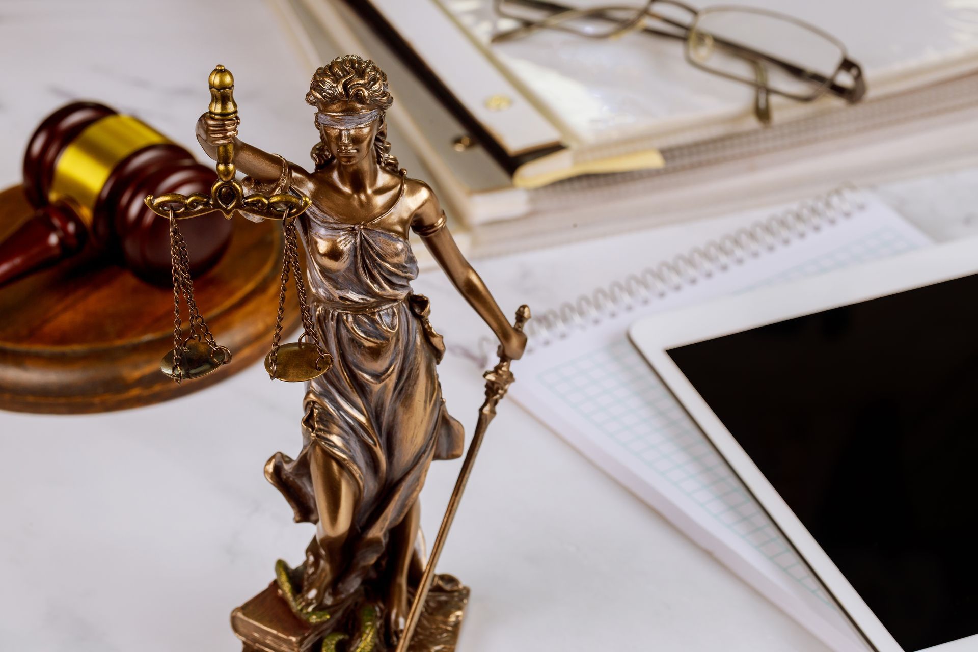 A statue of lady justice holding a gavel next to a tablet