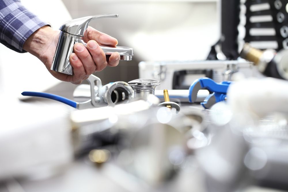 Plumber Holding A Chrome Faucet, Surrounded By Tools And Sink — DSR Plumbing Pty Ltd in Ashtonfield, NSW