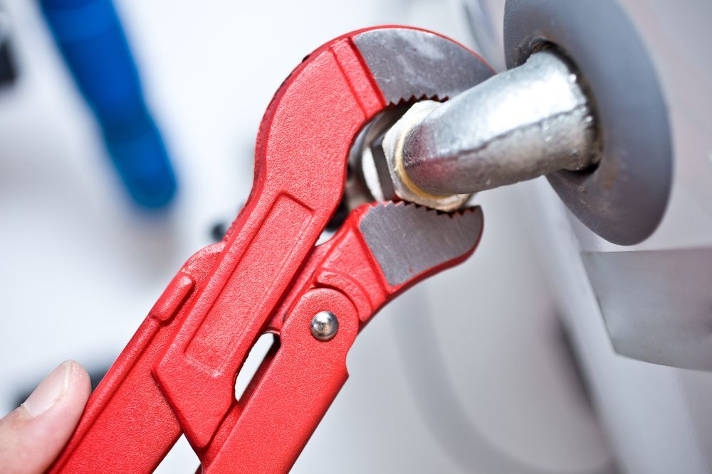 Red Pipe Wrench Tightening A Silver Pipe Fitting Against A White Surface — DSR Plumbing Pty Ltd in Newcastle, NSW