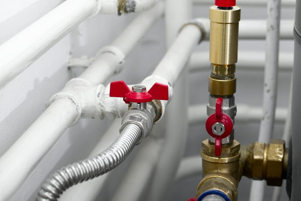 Close-up Of White Pipes With Red-handled Valves And Flexible Metal Hose — DSR Plumbing Pty Ltd in Newcastle, NSW