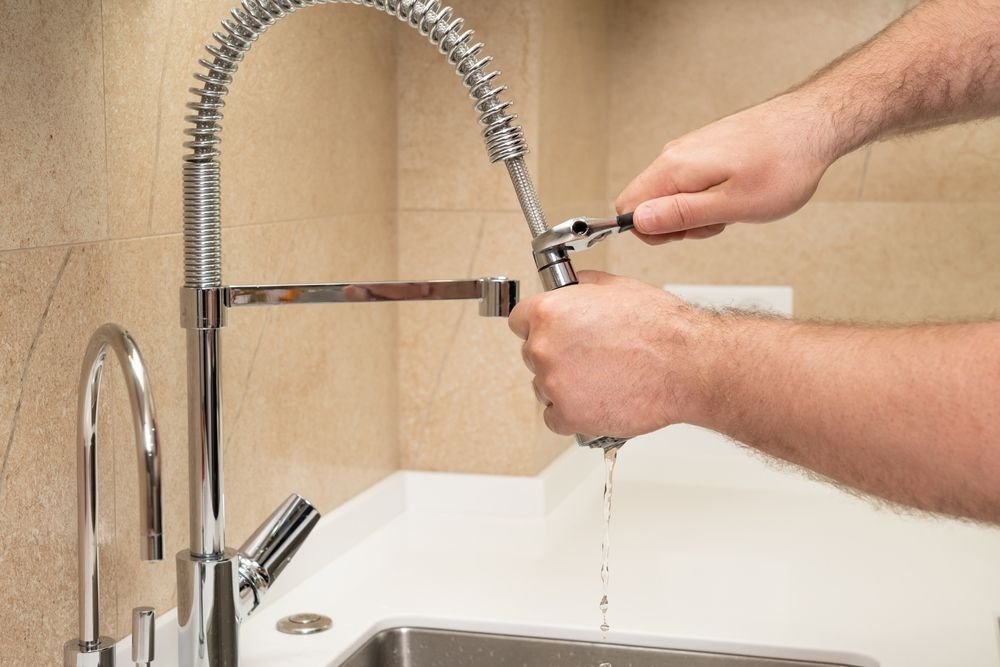 Person Using A Wrench To Repair A Kitchen Faucet — DSR Plumbing Pty Ltd in Newcastle, NSW