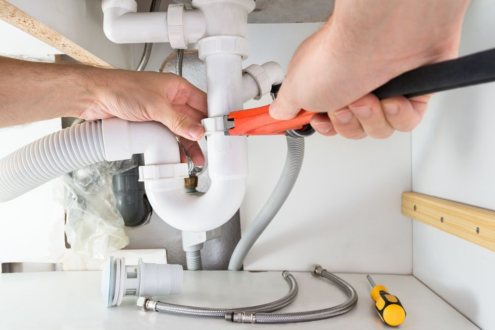 Plumber Using A Wrench To Repair White Pipes Under A Sink — DSR Plumbing Pty Ltd in Lake Macquarie, NSW