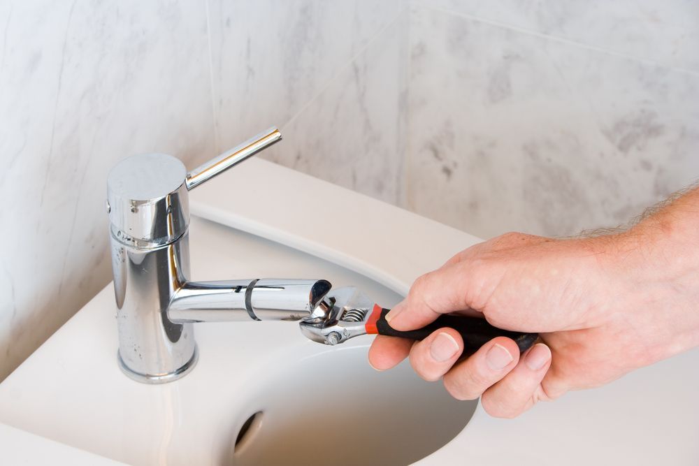 Hand Tightening A Wrench On A Shiny Faucet In A White Sink — DSR Plumbing Pty Ltd in Cessnock, NSW