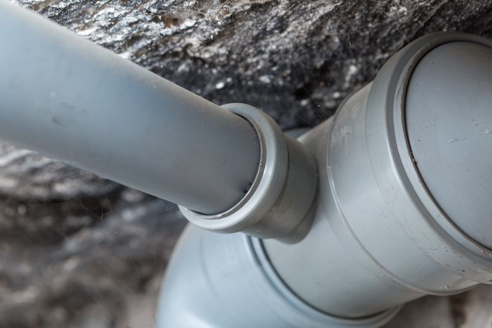 Gray Plastic Pipes Connected At An Angle Against A Rough — DSR Plumbing Pty Ltd in Cessnock, NSW