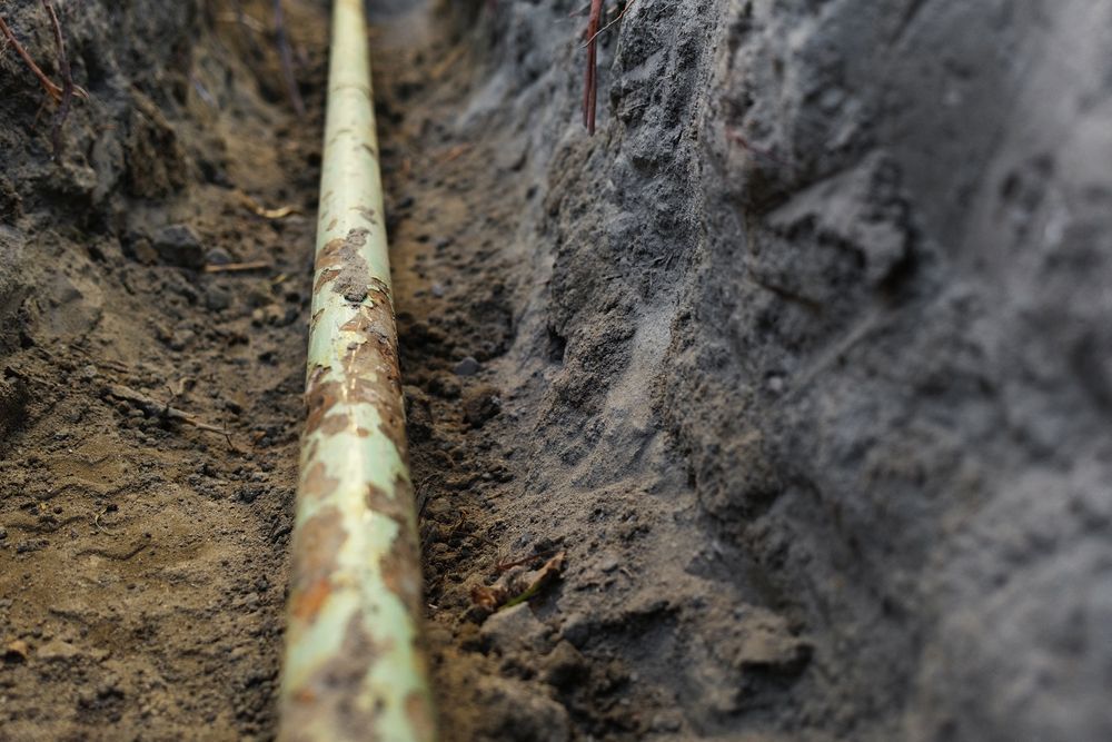Green Pipe Laid In A Narrow Trench Filled With Dirt — DSR Plumbing Pty Ltd in Lake Macquarie, NSW