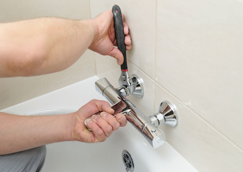 A Person Using A Wrench To Repair A Silver Bathtub Faucet — DSR Plumbing Pty Ltd in Cessnock, NSW
