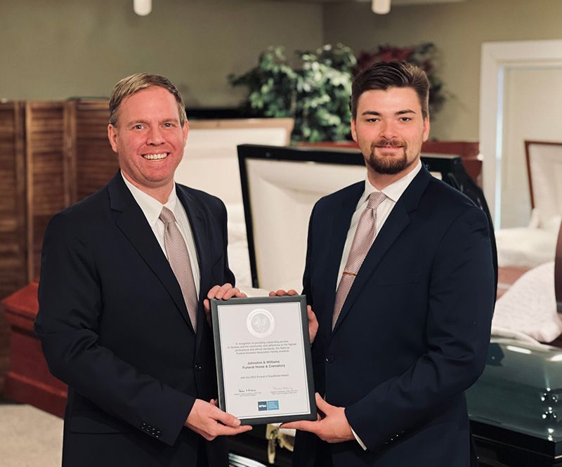 Henry D. Johnston, CFSP, owner of Johnston & Williams Funeral Home and Crematory (left) with Logan B. Henry, Intern Funeral Director & Intern Embalmer (right), displaying the firm's 2022 Pursuit of Excellence Award from the National Funeral Directors Association.