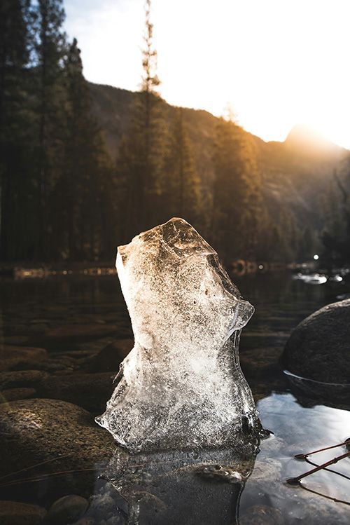 a large piece of ice is sitting in the water near a lake .