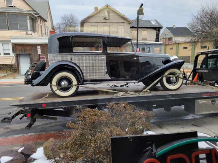 An old car is being towed by a tow truck