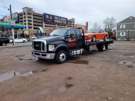 A tow truck with a car on the back is parked in a parking lot.
