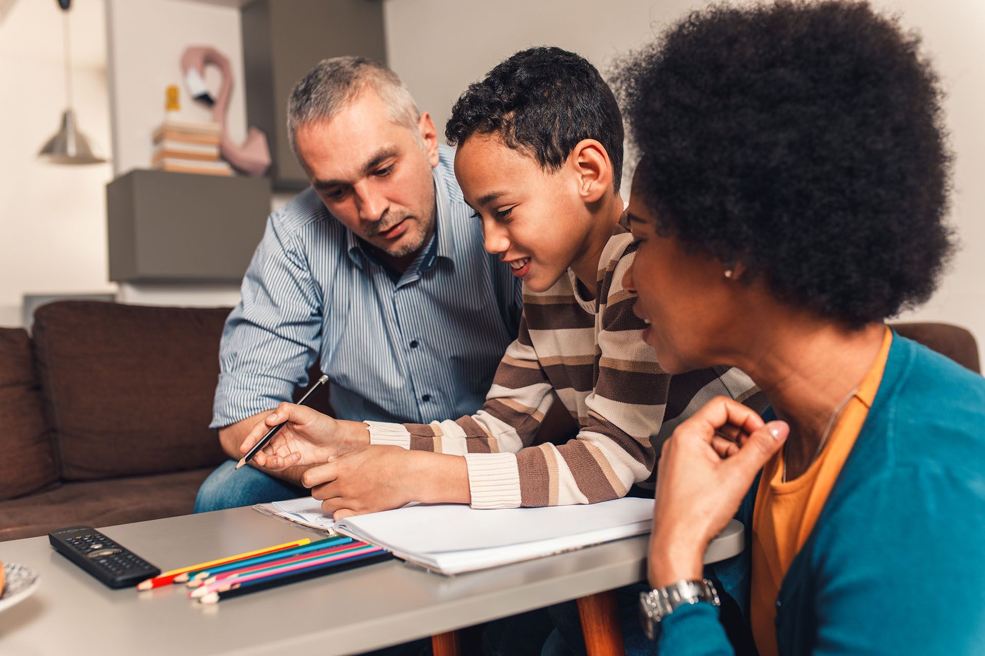 A man and a woman are helping a young boy with his homework.