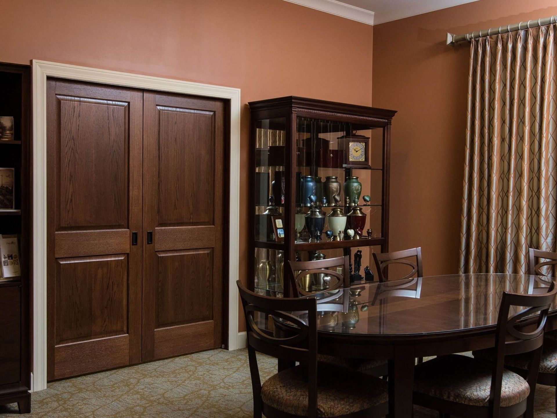 Dark wooden double doors with white trim in a dining room, brown walls, and a display cabinet.