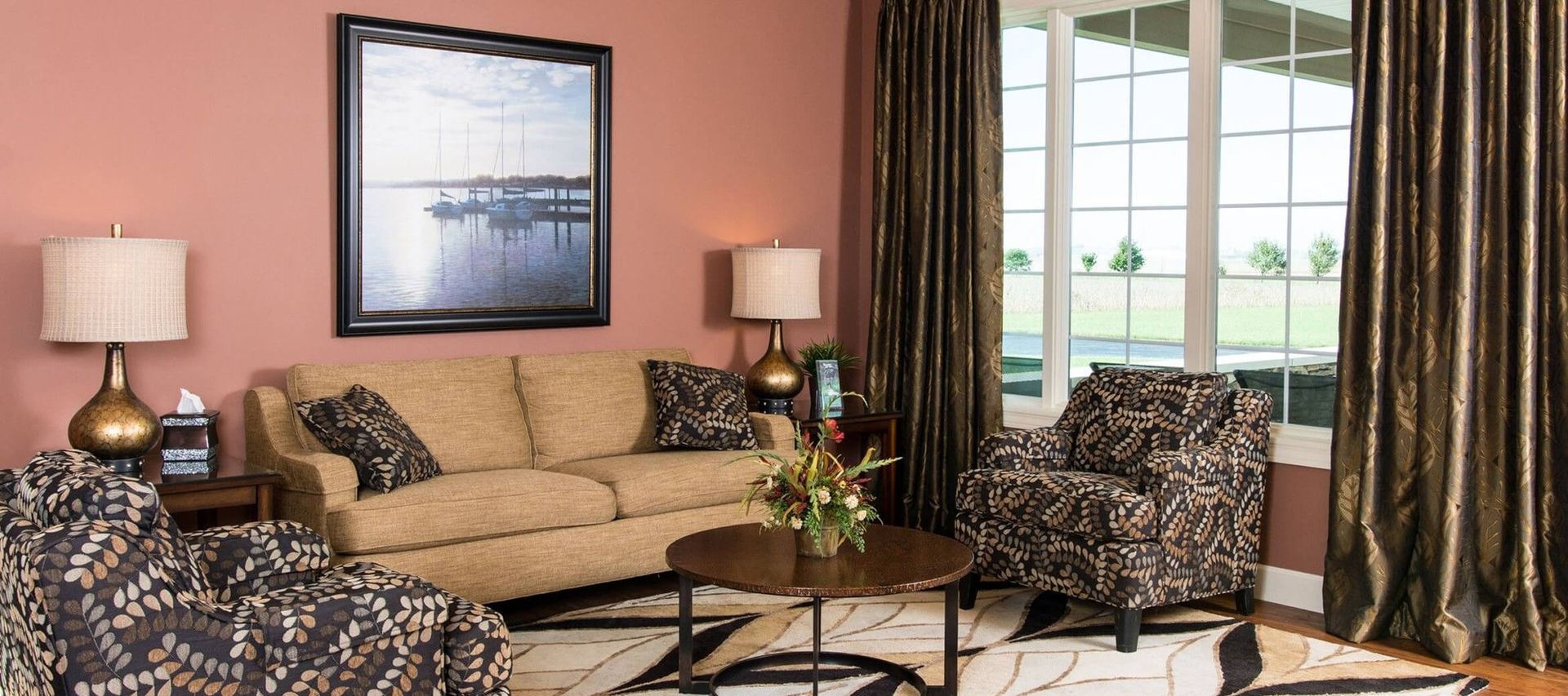 A living room with a beige sofa, patterned chairs, and a coffee table, against a pink wall with art and a window.