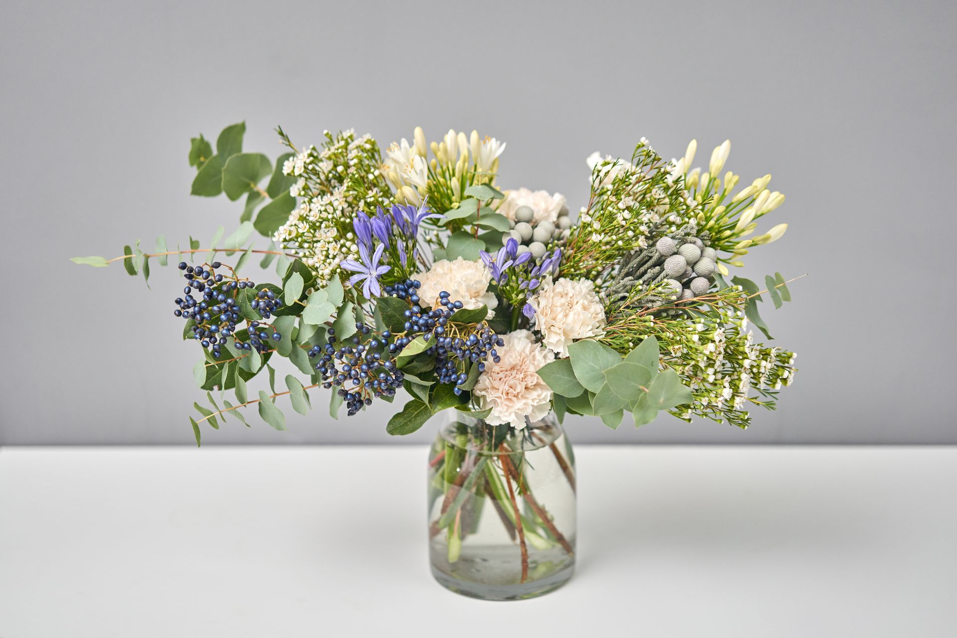 Bouquet of various flowers in a glass vase on a white table.