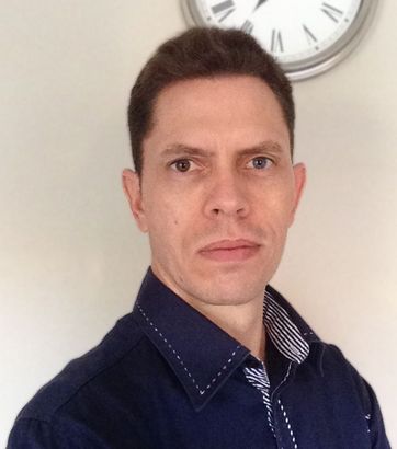 A man in a blue shirt is standing in front of a clock