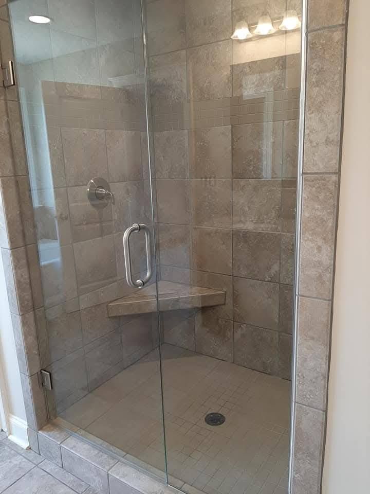 A shower stall with a glass door and a bench in a bathroom.