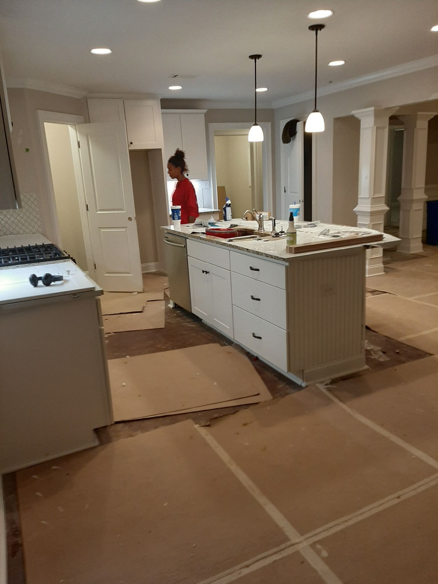 A woman in a red shirt is standing in a kitchen under construction.