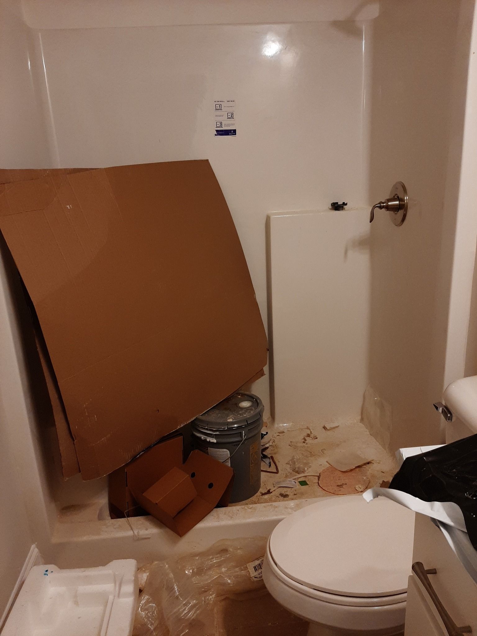 A bathroom with a toilet , shower , and cardboard box on the floor.