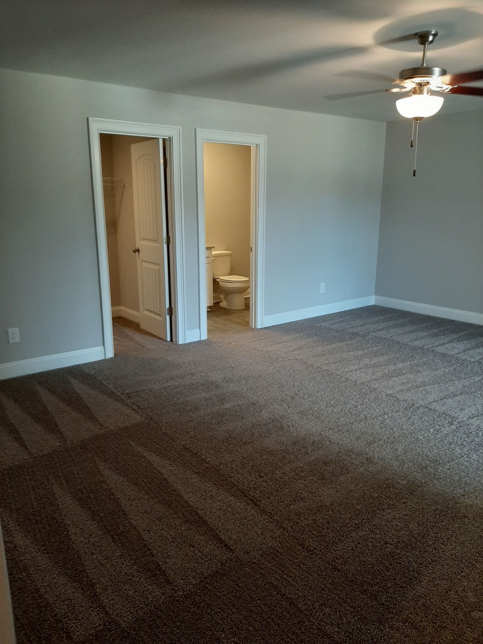 An empty room with a ceiling fan and a toilet.