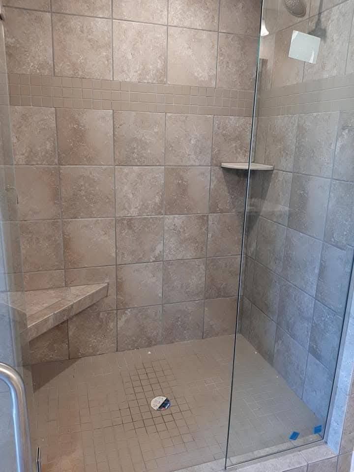 A walk in shower with a glass door and a bench.