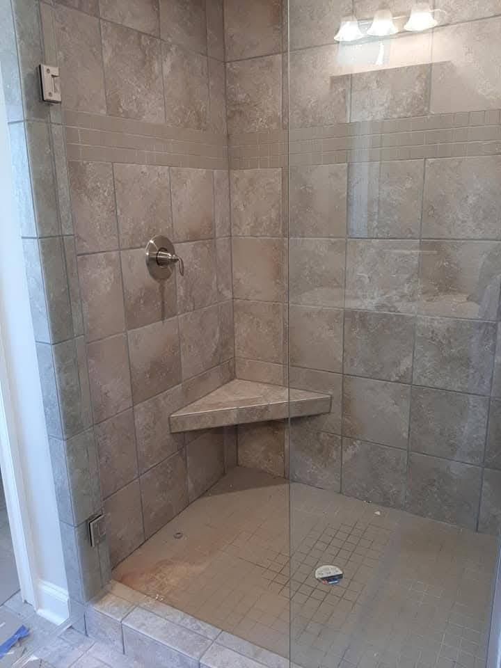 A walk in shower with a glass door and a corner seat.