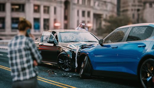Two cars crashed head-on on a city street, with a person standing nearby.